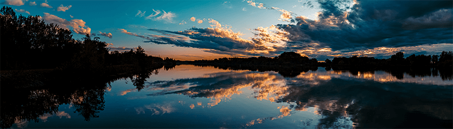 sunset view of landscape with lake, trees, and clouds