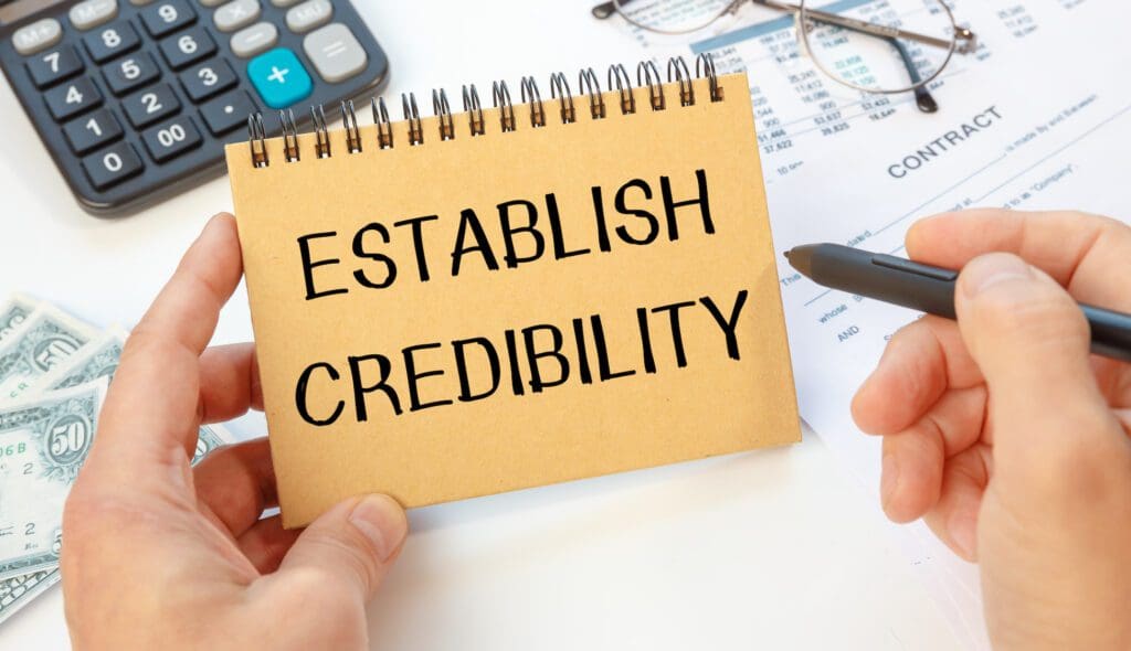 Notebook with text ESTABLISH CREDIBILITY near office supplies. Establishing Credibility