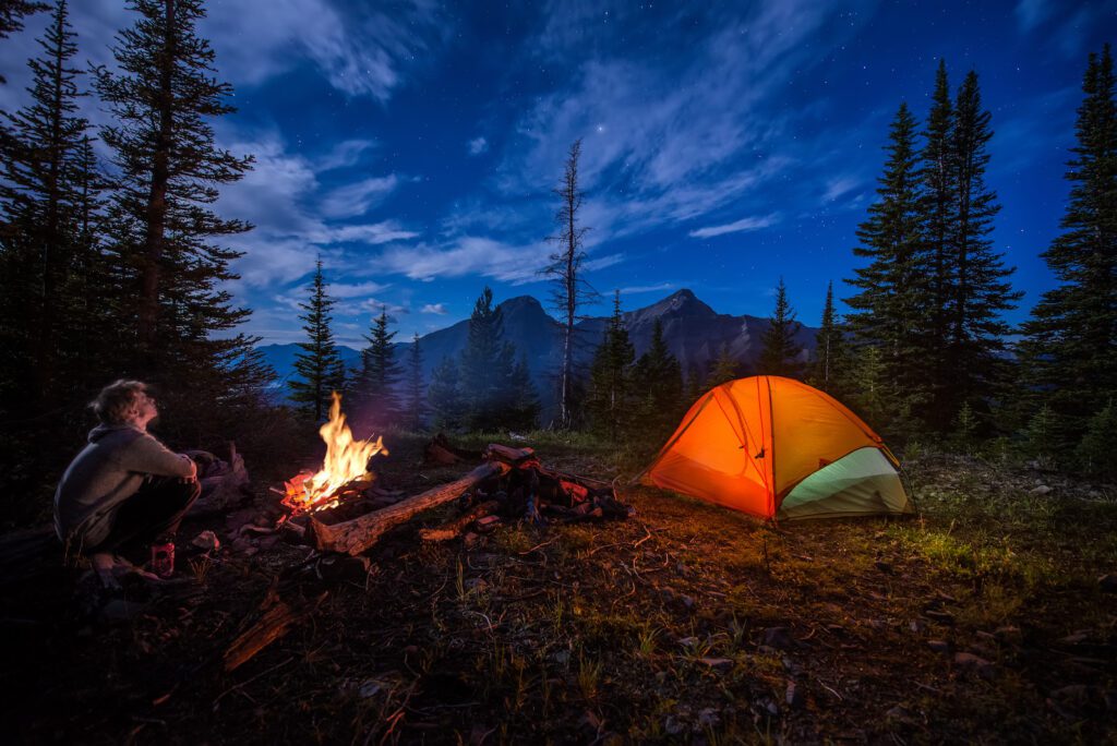 Man looking up at stars next to campfire and tent at night | Campsite Website Design